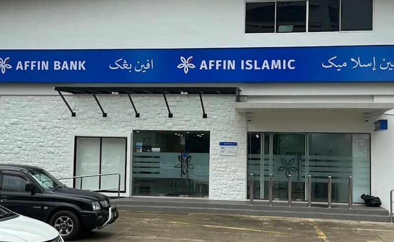 Pandangan hadapan cawangan AFFIN Bank Kuala Terengganu dengan papan tanda biru yang memaparkan tulisan rumi dan jawi. Bangunan mempunyai dinding batu putih, pintu kaca bercorak logo bank, serta kereta yang diletakkan di bahagian hadapan