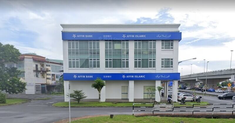 Sebuah pandangan dari jalan raya menunjukkan bangunan AFFIN Bank Prince Commercial Centredan Affin Islamic dengan dua tingkat dan fasad putih, di tengah-tengah bandar dengan pohon-pohon hijau di sekitarnya dan jembatan layang di kejauhan di sebelah kanan.