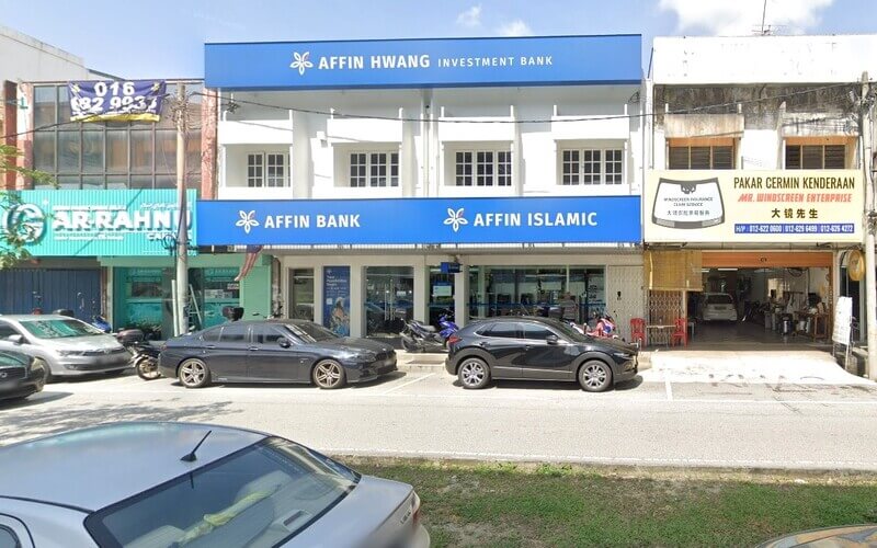 Pemandangan aras jalan bagi bangunan komersial putih yang memaparkan papan tanda biru untuk Affin Hwang Investment Bank di tingkat atas dan Affin Bank dan Affin Islamic di tingkat bawah. Ia diapit oleh kedai pajak gadai Ar Rahnu di sebelah kiri dan pakar cermin depan di sebelah kanan, dengan beberapa kereta dan motosikal diletakkan di hadapan
