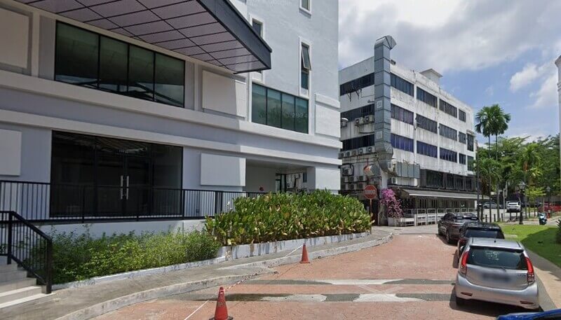 Pemandangan dari tepi jalan yang menunjukkan lokasi Affin Bank di Bukit Damansara, Malaysia, dengan sebuah bangunan kedai di sebelahnya dan beberapa kereta diparkir.