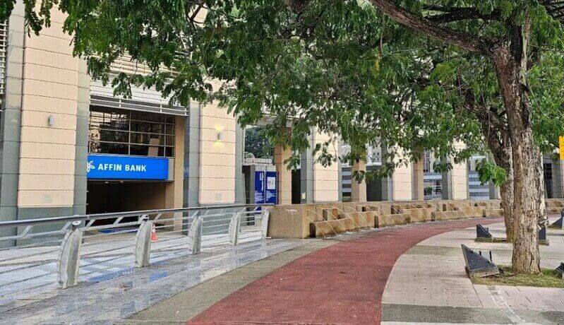 Pemandangan luar bangunan cawangan Affin Bank di Putrajaya dengan papan tanda biru, laluan pejalan kaki, dan pokok-pokok hijau.