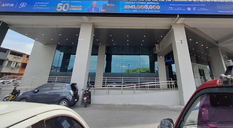 Pandangan hadapan cawangan bank AFFIN Bank Hikmah Exchange dengan dinding kaca pantulan biru, tiang konkrit putih, dan papan tanda kempen di atasnya.