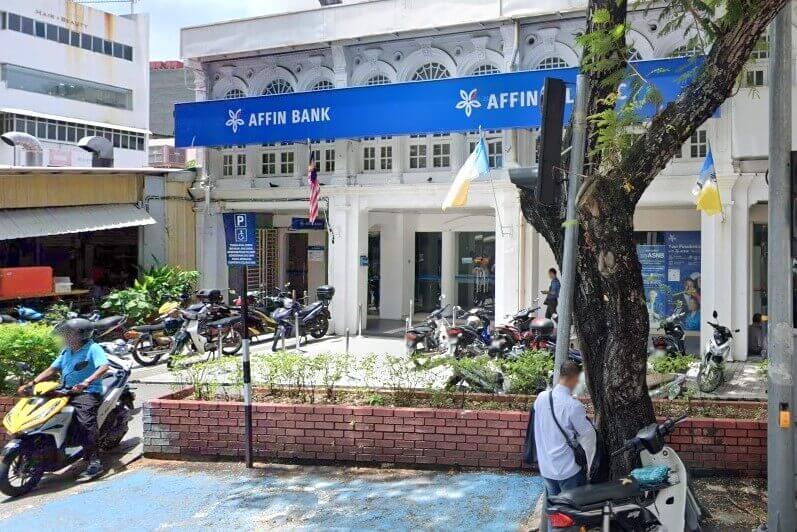 Pandangan luar cawangan Affin Bank di Jalan Macalister, George Town, terletak di dalam bangunan warisan gaya kolonial putih dengan papan tanda biru yang menonjol dan motosikal diletakkan di hadapan