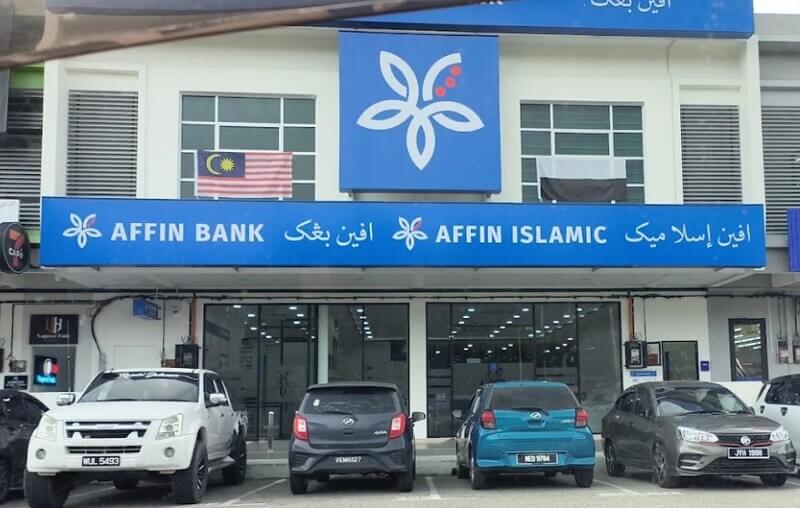 Pandangan hadapan cawangan bank AFFIN BANK Raub dengan bendera Malaysia dan Pahang terpapar di tingkap tingkat atas serta beberapa buah kenderaan diletakkan di petak letak kereta di hadapan premis