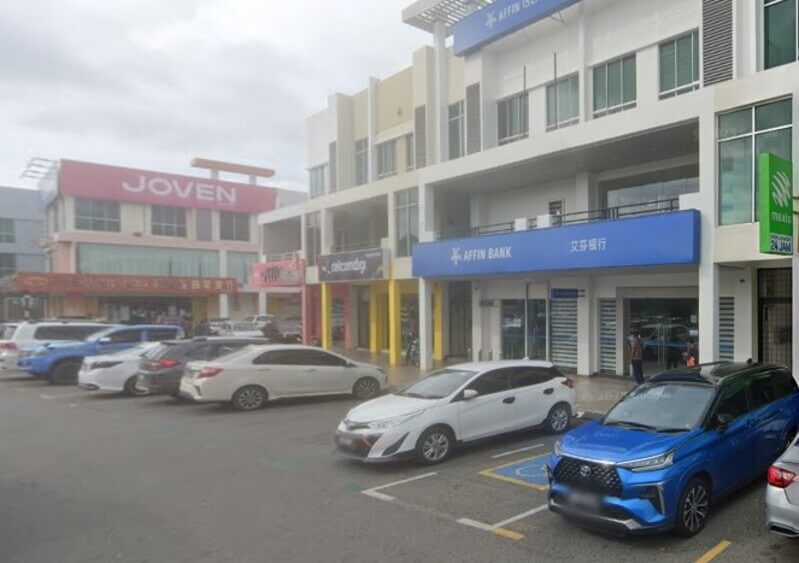 Pandangan luar premis kedai bertingkat di kawasan perniagaan yang menempatkan cawangan Affin Bank di Sandakan, premis CelcomDigi, dan JOVEN, dengan beberapa buah kereta diletakkan di tempat letak kereta di bahagian hadapan.