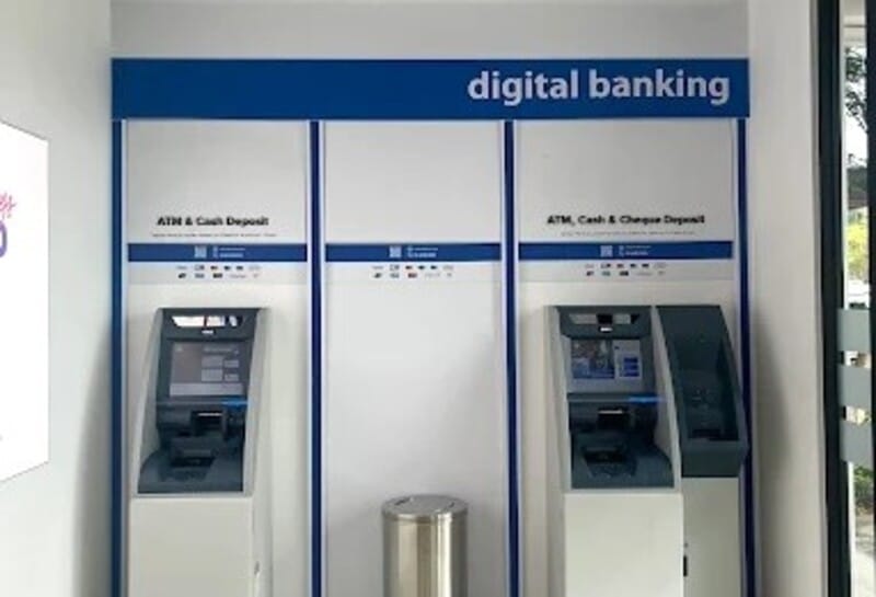 Bahagian dalam kios perbankan digital Affin Bank yang menampilkan dua mesin juruwang automatik (ATM) untuk deposit tunai dan cek, diletakkan pada dinding putih dan biru bersih dengan tong perak tengah