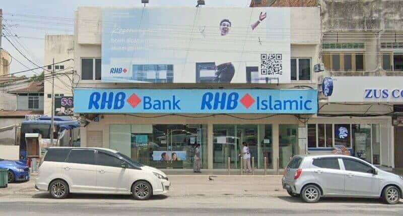 Pintu masuk hadapan bangunan RHB Bank Air Tawar menampilkan papan tanda biru besar dan papan iklan promosi di atas pintu masuk, dengan kereta diletakkan di hadapan