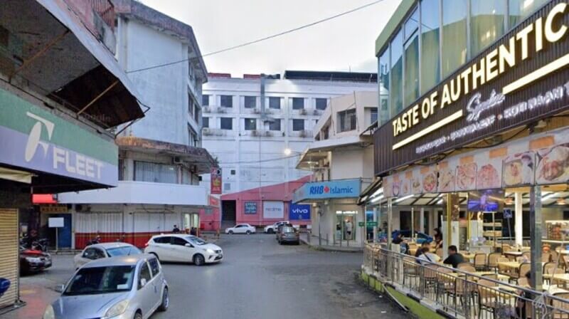 Pemandangan jalan perniagaan di Lahad Datu yang menunjukkan cawangan RHB Bank Lahad Datu, restoran TASTE OF AUTHENTIC, kedai FLEET, dan beberapa buah kereta diparkir di tepi jalan