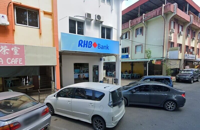 Pemandangan luar cawangan RHB Bank Lawas di bangunan kedai dua tingkat dengan papan tanda biru tertera "RHB Bank", serta beberapa buah kereta diletakkan di bahagian hadapan jalan
