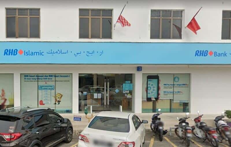 Pandangan luar Bank RHB dan cawangan RHB Islamic di Pasir Mas, menampilkan papan tanda biru muda dengan tulisan Jawi, kereta yang diletakkan dan motosikal di hadapan bangunan