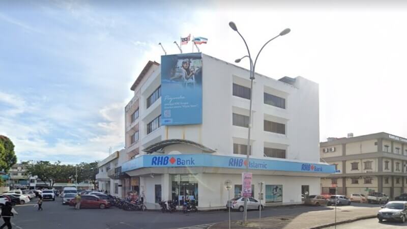 Pemandangan luar bangunan RHB Bank Tawau dan RHB Islamic berwarna putih di sudut jalan pada waktu siang.