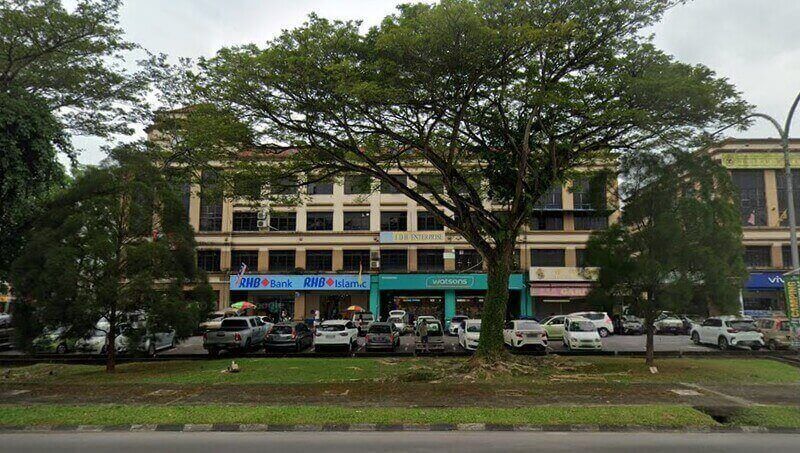 Pandangan hadapan bangunan kedai bertingkat yang menempatkan cawangan RHB Bank, RHB Islamic, dan premis Watsons di Batu Kawah, dengan barisan kereta di ruang letak kenderaan dan pokok besar di bahagian hadapan.