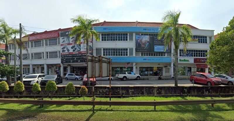 Pandangan luar bangunan kedai tiga tingkat yang menempatkan cawangan RHB Bank Kemaman dengan kenderaan diletakkan di hadapan dan pokok kelapa sawit/kelapa di bahu jalan