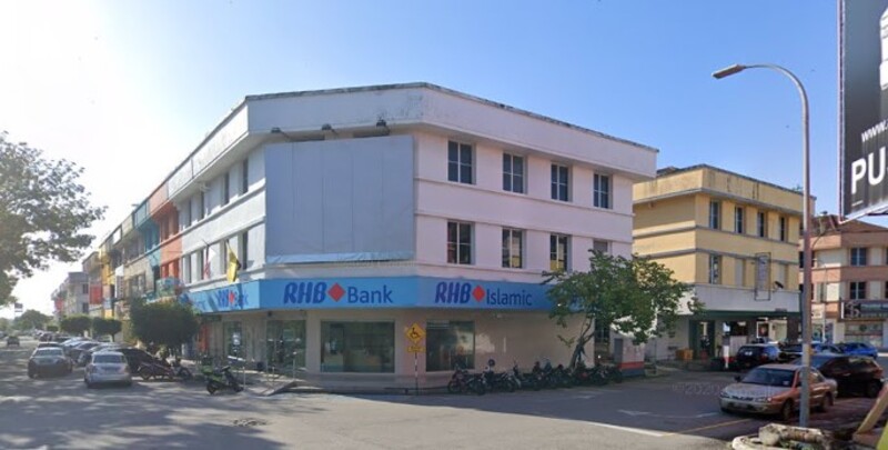 Pemandangan luar cawangan RHB Bank di Teluk Intan pada waktu siang, terletak di bangunan komersial bertingkat putih dan biru dengan tempat letak kereta aras jalan