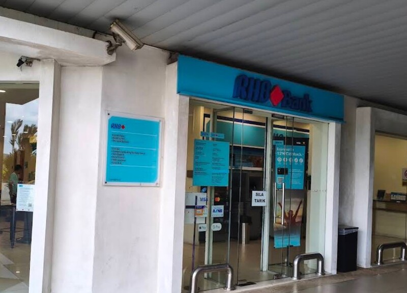 Pintu masuk cawangan RHB Bank Bintulu yang menampilkan pintu kaca automatik dengan pelekat bertulis "SILA TARIK", papan tanda biru berlogo RHB Bank di bahagian atas, serta papan maklumat waktu operasi dan poster promosi di bahagian dinding dan cermin premis