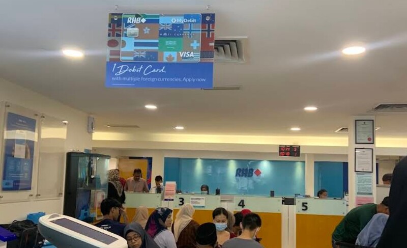 Suasana di dalam cawangan RHB Bank Butterworth yang sibuk dengan pelanggan di kaunter perkhidmatan di bawah papan tanda promosi kad debit RHB Multi Currency