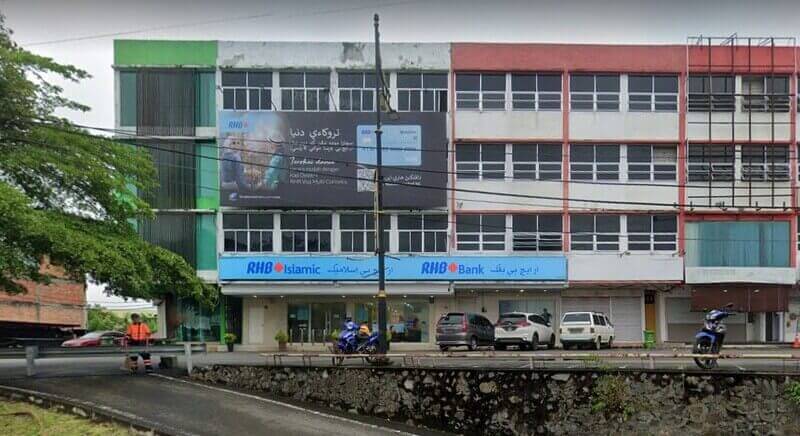 Bahagian luar Bank RHB dan cawangan RHB Islamic di Jerantut, Malaysia, terletak di bangunan komersial bertingkat dengan papan tanda Jawi yang boleh dilihat, kenderaan yang diletakkan dan papan iklan promosi yang besar di bahagian hadapan