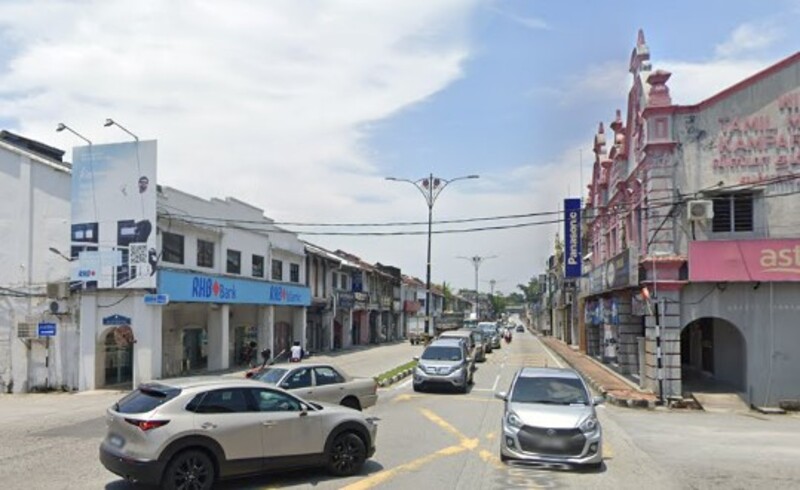 Pemandangan jalan raya di Kampar dengan deretan rumah kedai, cawangan RHB Bank Kampar di sebelah kiri, dan kenderaan yang lalu-lalang.