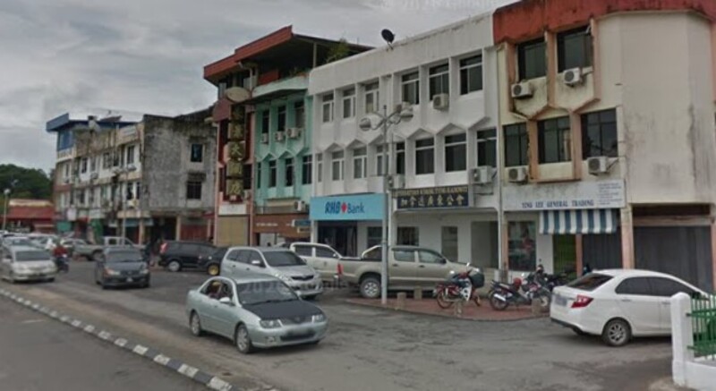 Pemandangan deretan bangunan kedai di sepanjang jalan raya, memaparkan cawangan RHB Bank dan beberapa perniagaan lain dengan kenderaan diletakkan di hadapannya.