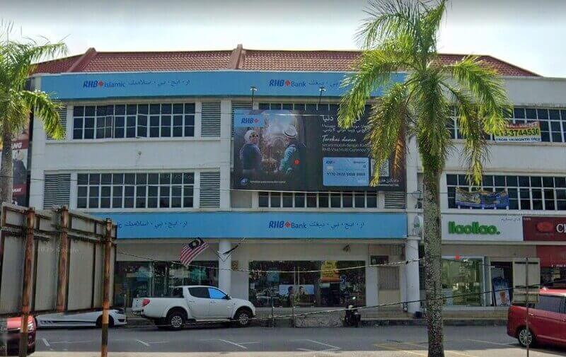 Pandangan luar cawangan RHB Bank dan RHB Islamic tiga tingkat di Kemaman, Malaysia, yang menampilkan papan tanda biru dengan tulisan Jawi, sepanduk promosi besar di bahagian hadapan, dan trak pikap putih yang diletakkan di hadapan