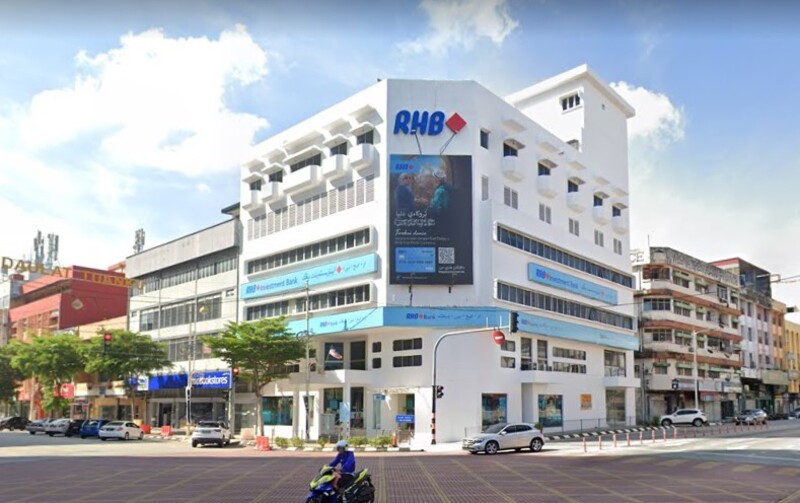 Bangunan RHB Bank Kuala Terengganu bertingkat di persimpangan jalan raya pada waktu siang dengan papan tanda "RHB" dan papan iklan besar di dinding luar