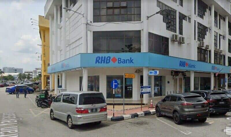 Pandangan luar Bank RHB dan cawangan RHB Islamic yang terletak di sudut jalan, memaparkan papan tanda biru yang menonjol di bangunan putih bertingkat dengan kereta yang diletakkan di hadapan