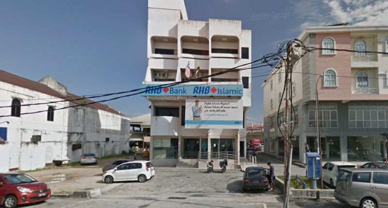 Pemandangan hadapan cawangan RHB Bank Sitiawan dan RHB Islamic yang beroperasi di sebuah bangunan putih bertingkat pada waktu siang yang cerah. Terdapat papan tanda utama bank, sepanduk iklan besar di bawahnya, serta bendera Malaysia yang diletakkan di balkoni.