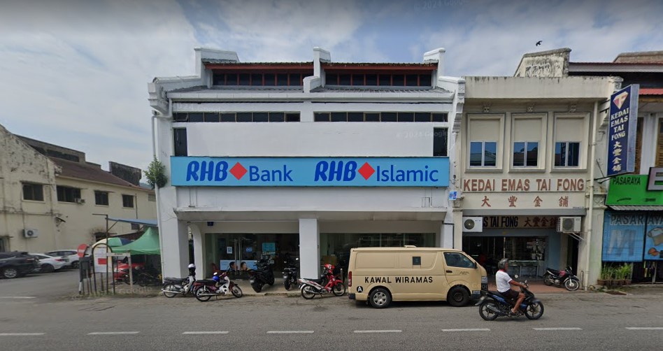 Pandangan hadapan bangunan cawangan RHB Bank dan RHB Islamic yang berwarna putih di sebuah deretan kedai. Terdapat sebuah van keselamatan dan beberapa buah motosikal diletakkan di kawasan parkir di hadapan bank