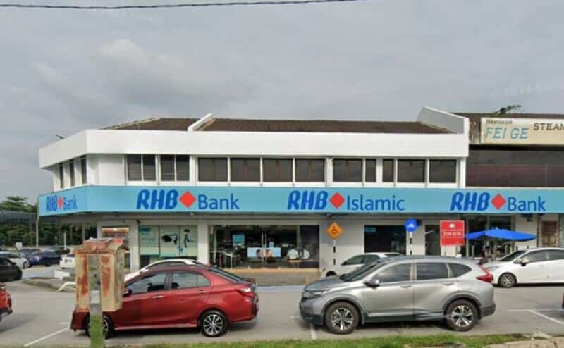Pandangan luar bangunan Bank RHB dua tingkat dan cawangan RHB Islamic dengan papan tanda biru, terletak di sudut jalan dengan kereta diletakkan di hadapan di bawah langit mendung
