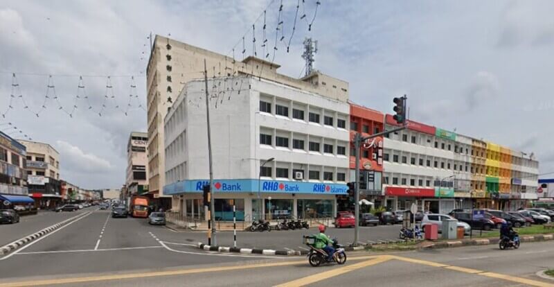 Pemandangan aras jalan bangunan RHB Bank bertingkat putih yang terletak di persimpangan sudut yang sibuk di Segamat, menampilkan jenama biru dan lot kedai berwarna-warni bersebelahan