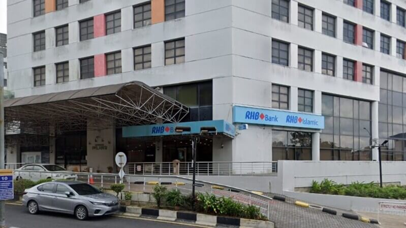 Pandangan luar cawangan RHB Bank di Taman Pelangi dan RHB Islamic di sebuah bangunan komersial, lengkap dengan papan tanda biru, laluan pejalan kaki, dan kereta yang diparkir di hadapannya