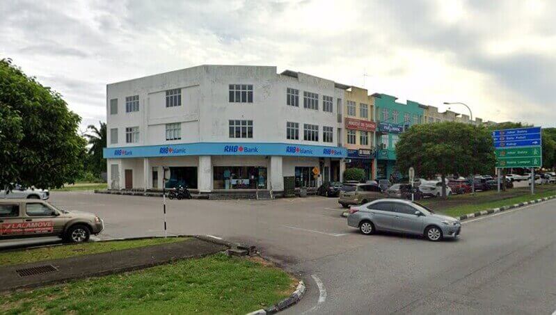 Pandangan luar sebuah bank RHB Bank dan cawangan RHB Islamic berwarna putih tiga tingkat yang terletak di sudut jalan di Pontian Kechil, menampilkan papan tanda biru dan bersebelahan dengan jalan utama dengan papan tanda lalu lintas berarah