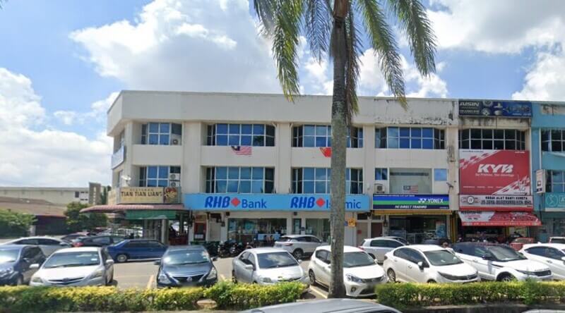 Pemandangan siang hari deretan rumah kedai tiga tingkat di Malaysia, menampilkan papan tanda RHB Bank Jalan Bakar Arang yang menonjol, bersama dengan papan tanda untuk Restoran Tian Tian Lian dan YONEX.