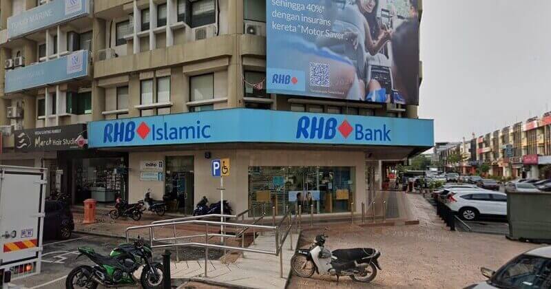 Gambar luaran sebuah unit sudut RHB Bank dan cawangan RHB Islamic di Bandar Baru Klang, Malaysia. Bangunan ini mempunyai papan tanda biru muda dengan logo bank, papan iklan promosi besar untuk insurans motor di bahagian hadapan, dan pelbagai motosikal yang diletakkan di sepanjang laluan pejalan kaki di latar depan