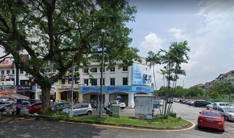 Pemandangan premis RHB Bank Bandar Sri Damansara dan RHB Islamic dari tepi jalan, terletak di bangunan rumah kedai bertingkat dengan kawasan tempat letak kereta dan pokok-pokok di sekelilingnya.