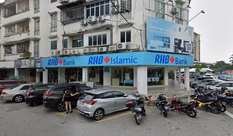 Pandangan luar cawangan RHB Bank dan RHB Islamic di tingkat bawah bangunan rumah kedai dengan kawasan tempat letak kereta dan motosikal di hadapannya.