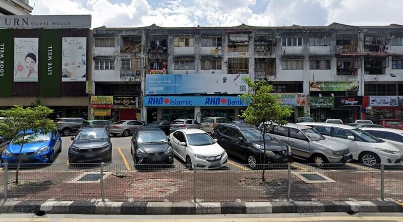 Barisan kedai tiga tingkat menunjukkan cawangan RHB Islamic dan RHB Bank dengan kawasan tempat letak kereta di hadapannya.