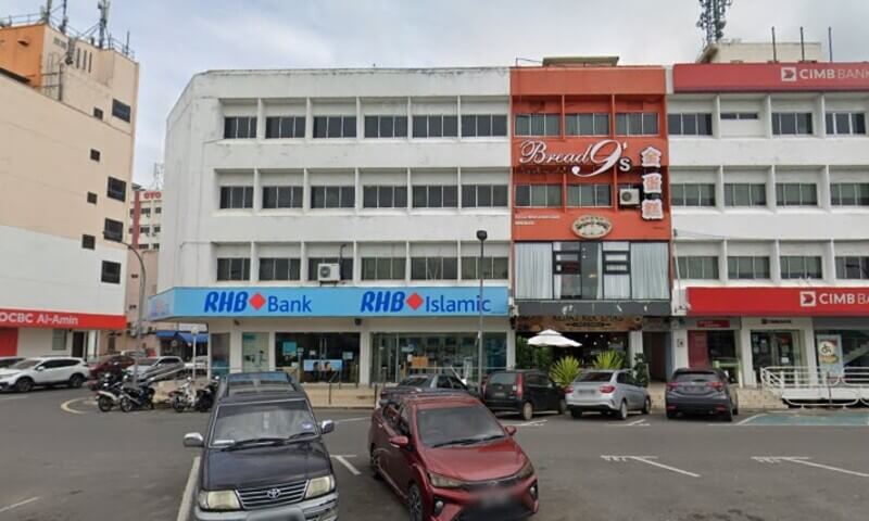 Pemandangan luar cawangan RHB Bank dan RHB Islamic di sebuah premis rumah kedai bertingkat bersama deretan kedai lain seperti Bread 9's dan CIMB Bank, lengkap dengan kawasan tempat letak kereta di hadapannya.