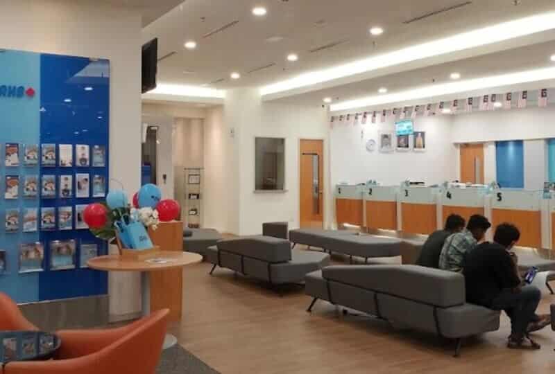 Bahagian dalaman moden cawangan RHB Bank di Bangsar Shopping Centre, menampilkan ruang menunggu yang luas dengan tempat duduk modular kelabu, lantai bertekstur kayu dan kaunter perkhidmatan dengan stesen juruwang bernombor di bawah