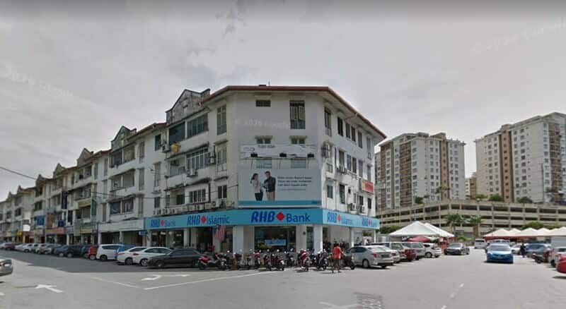 Pandangan luar Bank RHB dan cawangan RHB Islamic yang terletak di tingkat bawah bangunan rumah kedai sudut berwarna putih di Bandar Baru Ampang, menampilkan tempat letak kereta tepi jalan dan pangsapuri tinggi di latar belakang