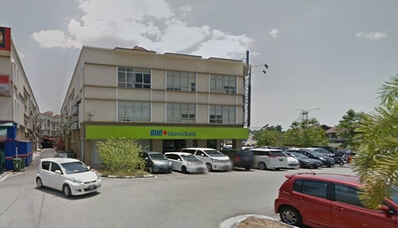 Pemandangan luar bangunan cawangan RHB Islamic Bank tiga tingkat di Bandar Baru Bangi, menampilkan papan tanda kedai berwarna hijau terang dan beberapa buah kereta diletakkan di latar depan di bawah langit yang cerah