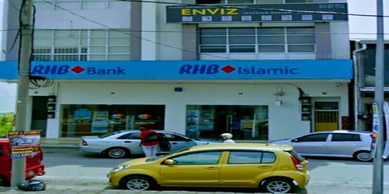 Pemandangan luar cawangan RHB Bank Banting dan RHB Islamic yang terletak di bangunan bertingkat. Papan tanda biru dipaparkan dengan jelas di atas tingkap kaca besar, dengan beberapa kereta diletakkan di sepanjang jalan di hadapan pintu masuk