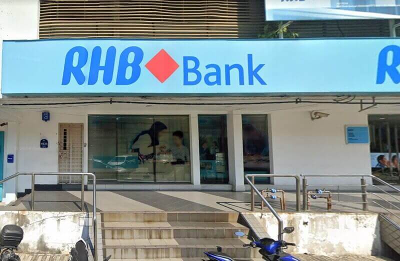 Kedai luaran cawangan RHB Bank yang menampilkan papan tanda biru muda yang besar dengan logo bank, pintu masuk kaca dengan poster promosi dan tangga pendek menuju ke pintu masuk