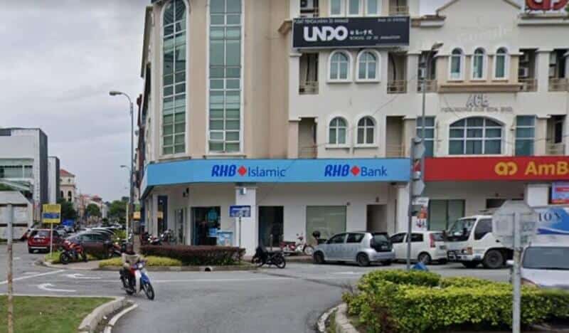 Pandangan luar Bank RHB dan cawangan RHB Islamic yang terletak di sudut jalan di Kota Damansara, memaparkan papan tanda kedai biru yang menonjol dengan perniagaan bersebelahan dan kenderaan yang diparkir