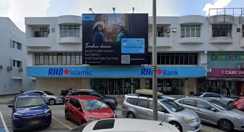 Pandangan luar cawangan RHB Bank dan RHB Islamic di Taman Megah, memaparkan papan iklan atas bumbung yang besar yang mengiklankan Kad Debit Pelbagai Mata Wang RHB Visa di atas papan tanda hadapan kedai berwarna biru
