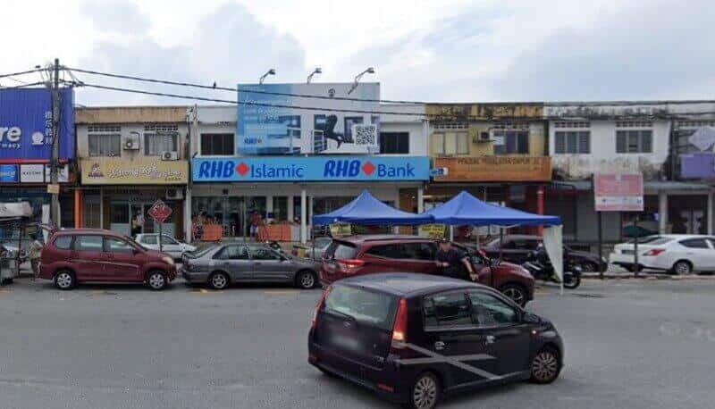 Pemandangan jalan bersudut lebar sebuah cawangan RHB Bank dan RHB Islamic yang terletak di deretan rumah kedai dua tingkat di Taman Suntex, Malaysia, dengan beberapa kereta diletakkan di hadapan