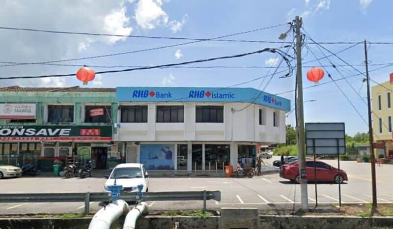Sebuah bangunan sudut dua tingkat berwarna putih yang memaparkan papan tanda Bank RHB dan RHB Islamic Cawangan Tanjung Karang. Ia terletak bersebelahan dengan kedai Econsave dan tempat letak kereta berturap dengan beberapa buah kereta di bawah langit yang cerah