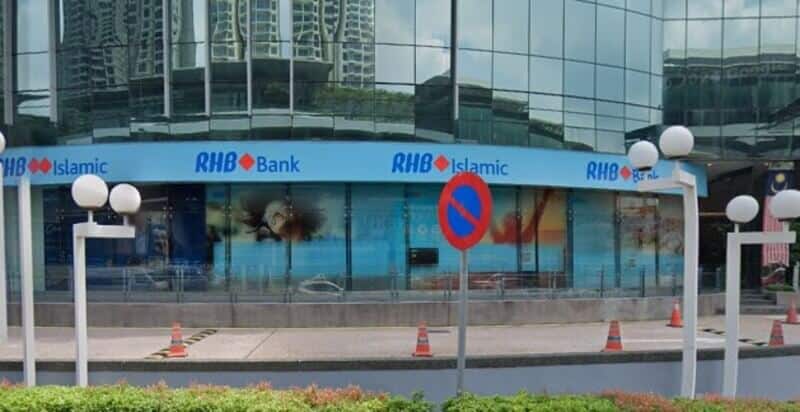 Pemandangan luar Bank RHB dan cawangan RHB Islamic di The Vertical, Bangsar South, menampilkan jalur papan tanda biru yang menonjol merentasi fasad kaca moden, dengan kon trafik dan lampu jalan di sepanjang tepi jalan