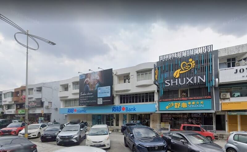Deretan bangunan kedai dua dan tiga tingkat di kawasan komersial dengan papan tanda cawangan RHB Islamic dan RHB Bank di Taman Megah berwarna biru di bahagian bawah, papan iklan besar di atasnya, serta pusat refleksologi Shuxin berhampiran