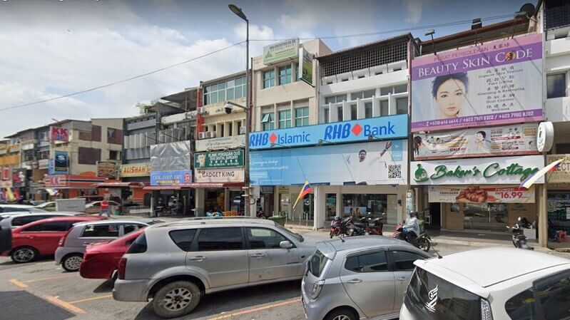 Pandangan luaran cawangan RHB Bank dan RHB Islamic di barisan kedai kawasan komersial bersama kedai-kedai lain seperti Baker's Cottage dan tempat letak kereta di hadapannya.